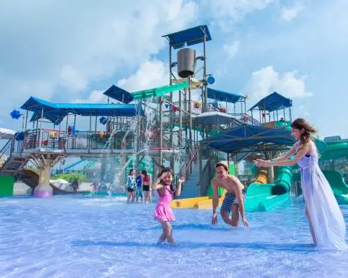 Children happily playing in the shallow water of the multi-level water play structure at Desaru Coast Adventure Waterpark, with parents supervising in the background.