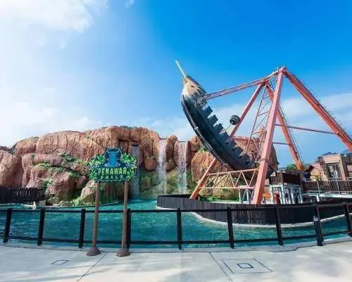 The thrilling pirate ship ride at Desaru Coast Adventure Waterpark, set against a backdrop of rock formations and a waterfall under a clear blue sky, inviting visitors to enjoy its swings.