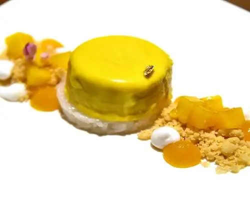 精緻的米其林星級芒果甜點，黃色慕斯搭配芒果丁和酥粒，在Pruek Cruise遊艇上呈現。