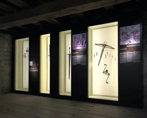 Inside Chillon Castle's exhibition hall, display cases feature hundreds of medieval archaeological artifacts like ancient swords and crossbows, offering insight into the castle's rich history.