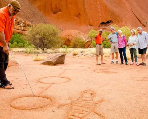 An Aboriginal guide illustrates rock art to tourists during an Uluru morning walk, sharing indigenous culture and heritage in Australia's Northern Territory.