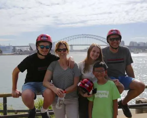 A family group poses by the water with the magnificent Sydney Harbour Bridge in the background, their Sydney bike tour filled with joy.
