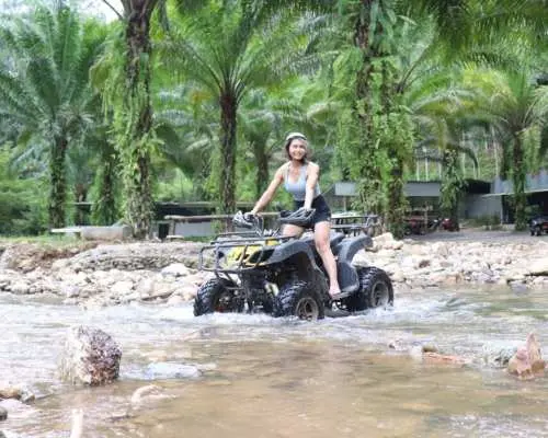 An adventurous woman wearing a helmet, riding an ATV through a shallow river in Phuket, enjoying the thrill of off-road exploration amidst tropical scenery.