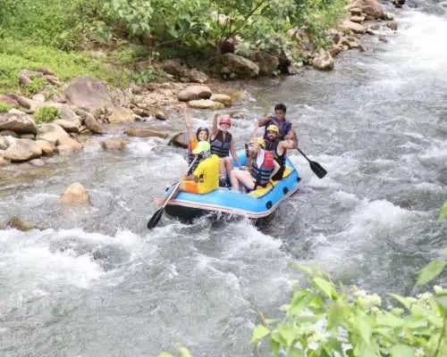 A group of enthusiastic travelers on a blue inflatable raft, paddling down a scenic river in Phuket, enjoying the guided whitewater rafting adventure.