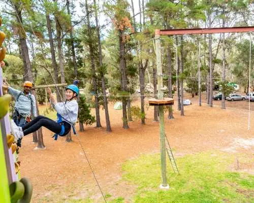 An instructor guides a young participant on the vibrant climbing wall at Southern Adventure Centre, South Australia, enjoying an exciting outdoor sport surrounded by beautiful bushland scenery.