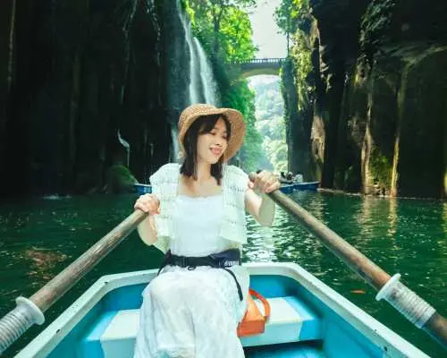 高千穂峡でボートに乗る観光客、緑豊かな崖と美しい真名井の滝を眺めながら、独特の峡谷体験を楽しむ様子。