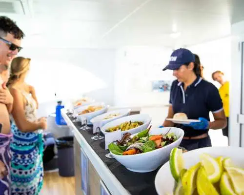 クルーズ船上で新鮮なサラダや美味しい料理を含む豪華なビュッフェランチを楽しむ観光客。クイーンズランドのイルカとタンガルーマ難破船ツアーでエネルギーを補給。