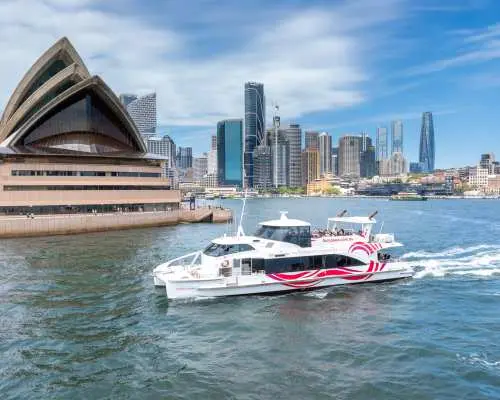 一艘雪梨港渡輪船票包含的庫克船長快速渡輪，行駛於湛藍海面，背景為雪梨歌劇院與宏偉的城市天際線。