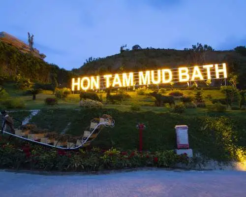ニャチャン・ホンタム島泥風呂の夜の入口、丘の中腹に巨大で光る「HON TAM MUD BATH」の看板があり、訪問者を歓迎しています。