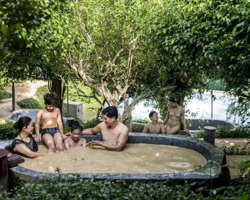 A family with children enjoying a joyful mineral mud bath experience amidst lush greenery at Hon Tam Island's mud bath area, Nha Trang.