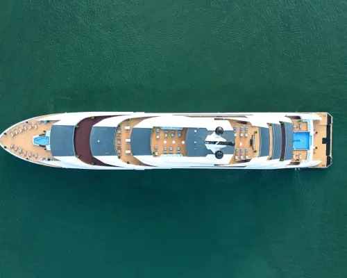 Top-down aerial view of the Ambassador luxury 5-star day cruise ship, highlighting its multiple spacious decks and sleek design as it navigates Halong Bay's emerald waters.