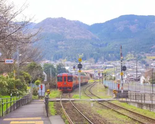 九州鄉間火車駛過鐵軌，遠處山巒疊翠，代表著SUNQ Pass巴士券能帶您探索九州的多元交通與風光。