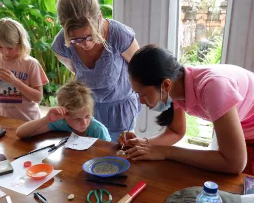 In a child-friendly Bali silver making workshop, an instructor guides adults and children creating together, highlighting the joy of family participation in crafting unique silver jewelry.