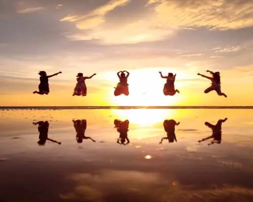 A group of friends synchronously jumping on Sabah's Sky Mirror beach at sunset, creating multiple dynamic silhouettes and perfect reflections, making joyful memories.