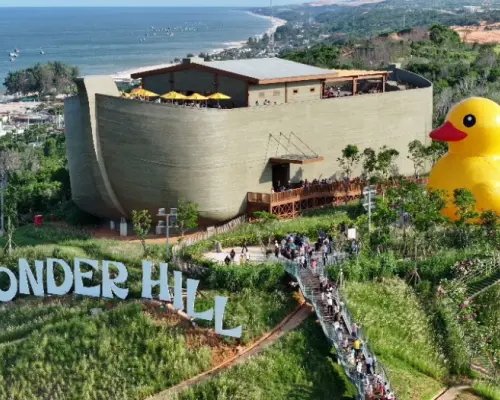 Khung cảnh hùng vĩ của Đồi Kỳ Diệu NovaDreams Phan Thiết, nổi bật với tòa nhà hình con thuyền Noah độc đáo và tượng vịt vàng khổng lồ, phía sau là vịnh biển quyến rũ.