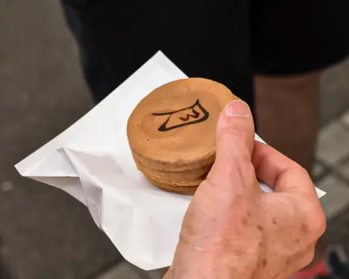 A hand holding a traditional Japanese Imagawayaki or Taiyaki sweet with a unique pattern, a delicious street food snack on the Tokyo Food Bike Tour.