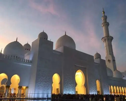 The majestic Sheikh Zayed Grand Mosque in Abu Dhabi glowing at dusk, with illuminated arches and domes creating a spectacular night view, a highlight of the city tour.