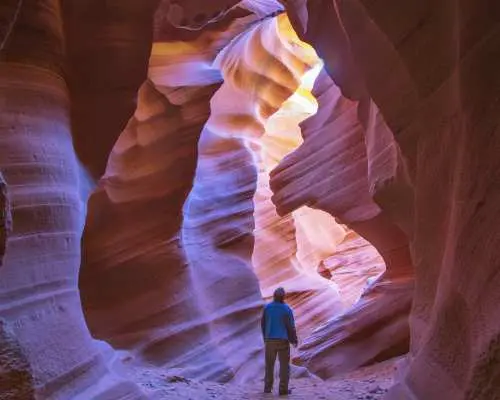 Travelers explore Lower Antelope Canyon, sunlight creating enchanting patterns through narrow sandstone slots, revealing unique geological wonders on this 8-day tour.