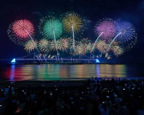 廣安里海水浴場的觀眾聚集欣賞2025釜山煙火節，廣安大橋上方的絢爛煙火與雷射燈光秀倒映海面。