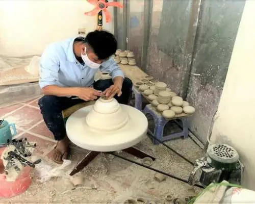 ベトナムのバッチャン村の陶芸工房で、マスクを着用した職人がろくろを使い、大型の陶器作品を丁寧に形作っています。