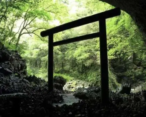 The mystical cave entrance of Amano Yasukawara in Takachiho, with a solemn Torii gate leading to a sacred path, a key spiritual power spot in Miyazaki.