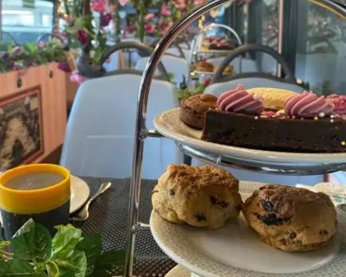 Exquisite three-tiered afternoon tea set on the London Taylor Swift themed double-decker bus, featuring freshly baked scones, pink frosted cakes, and pastries, alongside a warm drink.