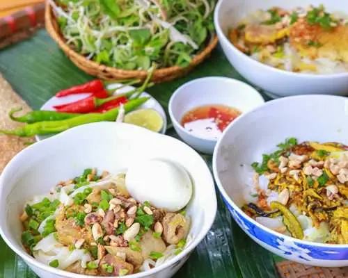 ダナンの名物麺料理「ミークアン」が数皿。新鮮なハーブ、唐辛子、ライスクラッカー添えで、本格的な地元ランチ体験。