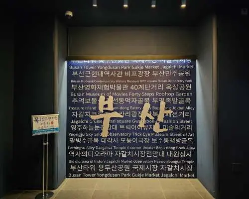 釜山塔內部走廊，牆面以韓文和英文展示釜山主要景點列表，並大字標示「BUSAN」，引導遊客探索城市。