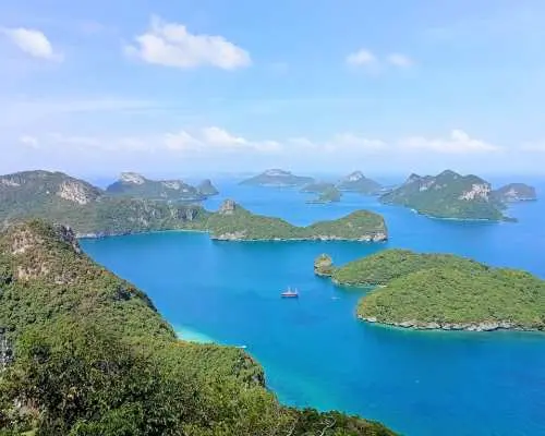 A breathtaking panoramic view of Angthong National Marine Park in Koh Samui, with numerous lush green limestone islands scattered across the vast blue ocean, a tour boat gently cruising.