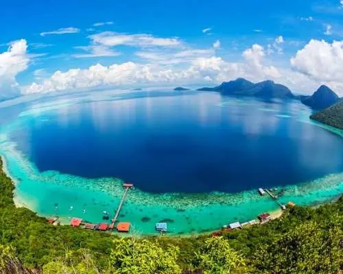 Stunning aerial view of Bohey Dulang's lagoon in Tun Sakaran Marine Park, Semporna, featuring mesmerizing blue waters, stilt houses, and vibrant coral reefs, ideal for snorkeling and diving.