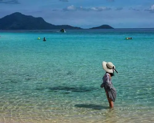 A tourist stands in the crystal-clear shallow waters of Sibuan or Mantabuan Island in Semporna, ready for snorkeling or beach relaxation during a Tun Sakaran Marine Park island hopping tour.
