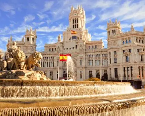 Madrid's grand Cybele Palace and Fountain at Cybele Square, with Spanish flags waving, an unmissable city landmark and historical monument on this enriching twin-city tour.