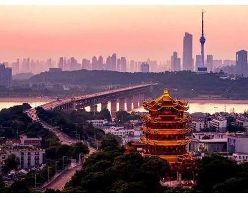 武漢黃鶴樓在黃昏時分的壯麗景色，橙紅色天空映襯著古老樓閣與現代城市天際線和長江大橋。