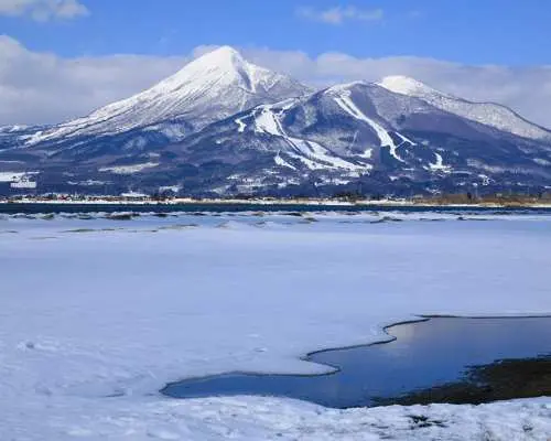 日本东北天镜湖冬季雪景，冰封湖面与远处雪峰相映，蓝天白云下呈现宁静壮丽的自然美景。