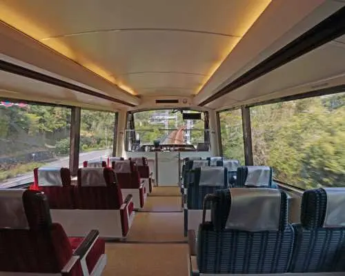 The spacious and comfortable interior of the Izu Kyuko Line Resort21 sightseeing train features large windows, offering picturesque views of the lush green scenery along the route.