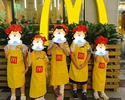 Trong hoạt động trải nghiệm nghề nghiệp cho trẻ em ở Thâm Quyến, một nhóm trẻ em mặc đồng phục McDonald's, hóa thân thành nhân viên phục vụ nhỏ, vui vẻ chụp ảnh trước logo chữ M khổng lồ.