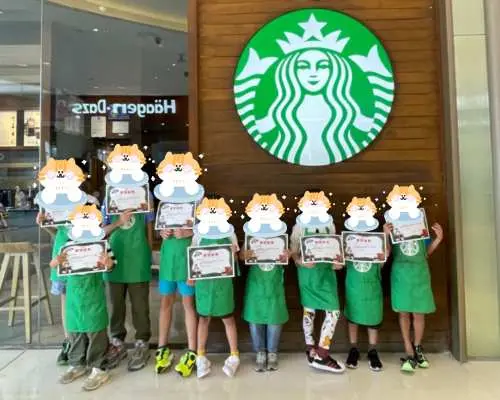 Trong hoạt động trải nghiệm nghề nghiệp cho trẻ em ở Thâm Quyến, một nhóm các barista nhỏ mặc tạp dề xanh, cầm giấy chứng nhận, vui vẻ chụp ảnh trước logo Starbucks sau khi hoàn thành trải nghiệm barista.