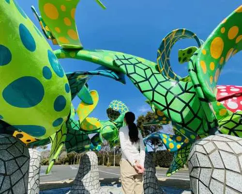 游客在鹿儿岛雾岛户外艺术博物馆，驻足欣赏标志性的鲜艳点点装置艺术，感受独特的秋日艺术文化体验。