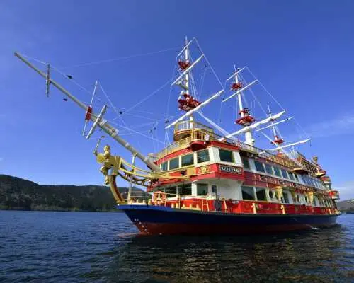 Japan Kanto private car tour, the Hakone Pirate Ship cruises on Lake Ashi, surrounded by majestic mountains and a clear blue sky, offering scenic beauty.