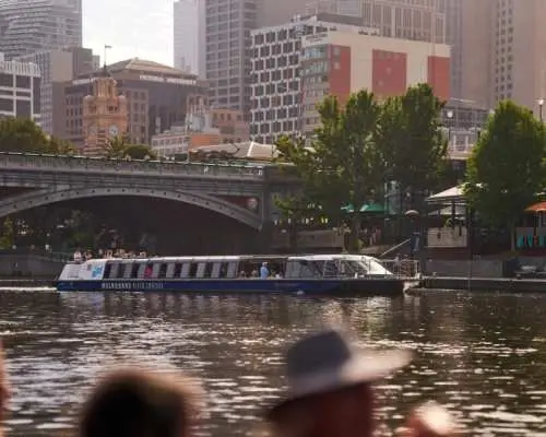 雅拉河游船缓缓通过历史悠久的拱桥，两岸是墨尔本繁华的城市建筑群，展现独特的河道视野。