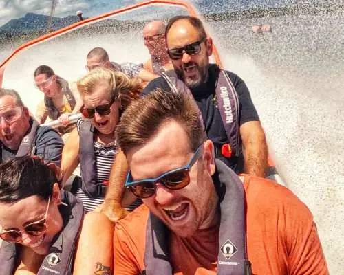 Excited passengers on the Bad Fishy jet boat, wearing life vests, getting soaked by splashes, laughing joyfully as they experience thrilling spins and splashes in Cairns' Trinity Inlet.