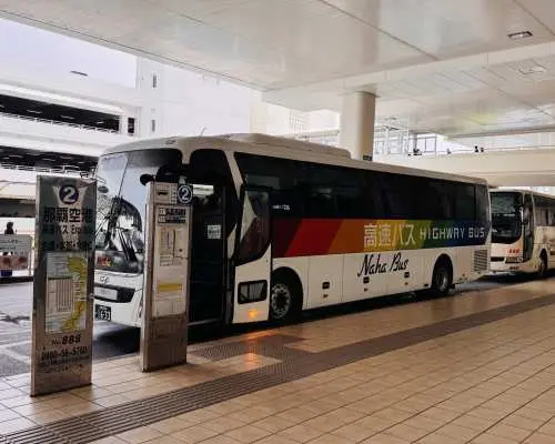 沖繩那霸機場高速巴士停靠站，一輛白色往返巴士可見，提供直達美麗海水族館的便捷交通服務。