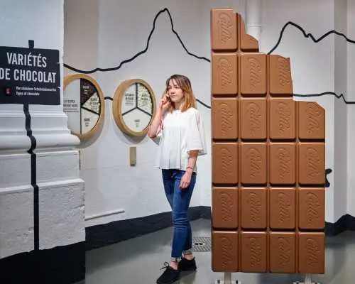 A visitor exploring the interactive exhibit at Maison Cailler chocolate museum, admiring a giant chocolate bar display and learning about diverse Swiss chocolate flavors.