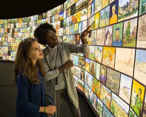 梵谷博物館內，遊客們在弧形數位牆前觀看梵谷畫作展示，透過高科技互動體驗，深入了解藝術家的生平與作品。