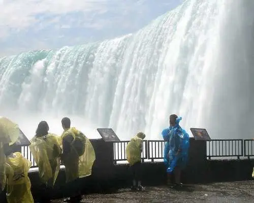 Tourists in ponchos stand on a viewing platform at Canada's Niagara Falls, witnessing the powerful Horseshoe Falls up close, feeling the awe-inspiring force of the cascading water.