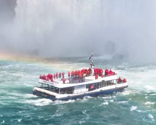 The Hornblower boat at Canada's Niagara Falls, filled with tourists in red ponchos, intimately experiences the majestic cascade and mist, a true natural wonder.