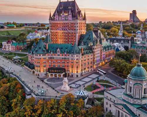 An aerial view of Quebec City at dusk, featuring the iconic Fairmont Le Château Frontenac majestically lit by the sunset, highlighting Eastern Canada's European-style old town charm.