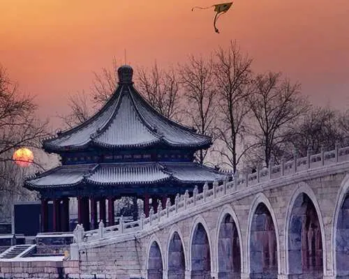 베이징 이화원의 상징적인 십칠공교와 고전적인 정자의 파노라마 전경, 고요한 겨울 일몰에 포착되어 정원 예술의 아름다움을 강조합니다.