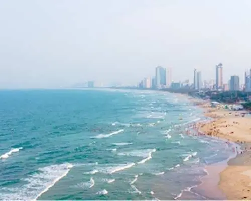 다낭 미케 해변의 광활한 조감도. 넓은 모래사장, 잔잔한 파도의 에메랄드빛 바다, 활기찬 도시 스카이라인이 어우러진 최고의 서핑 명소입니다.