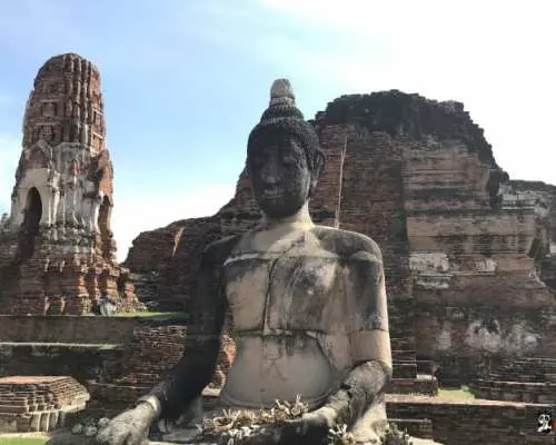 アユタヤの歴史的な寺院で、風化した座仏像が古代のレンガ造りの遺跡を背景に佇む。かつての王国の栄光を今に伝えています。